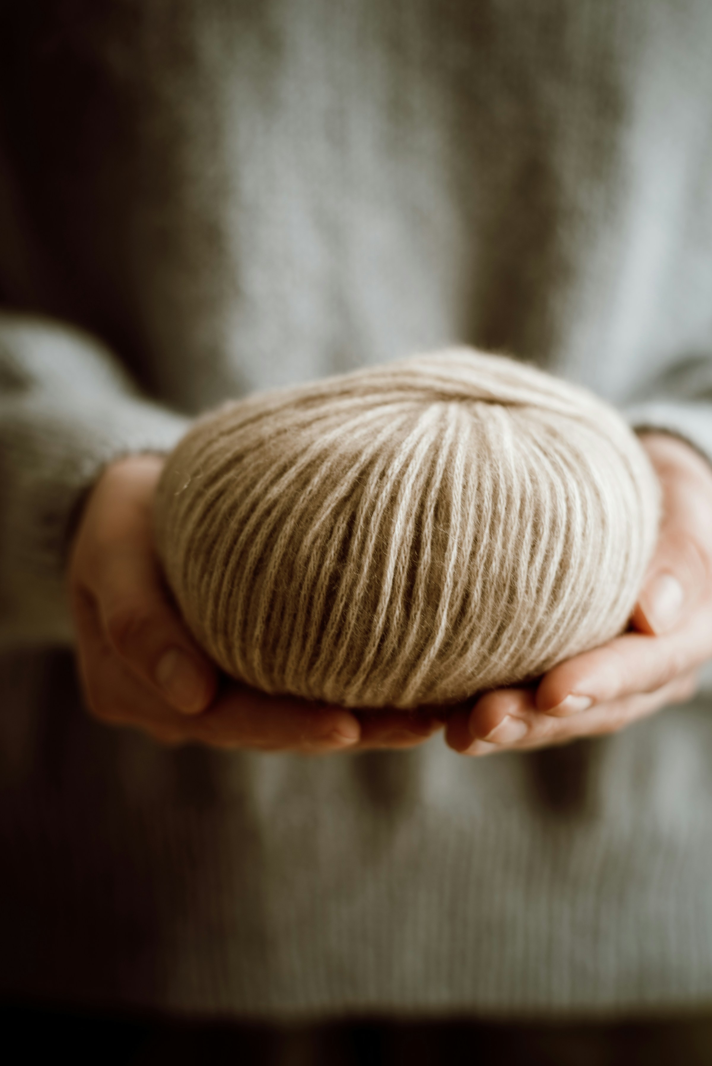 A ball of natural cream-coloured yarn held in two hands against a soft knit sweater.